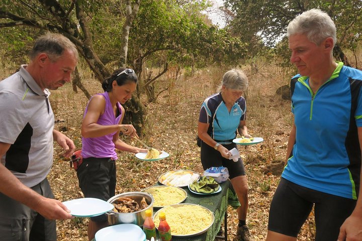 Group of four cyclists serving themselves food from a table in a natural setting.