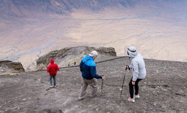 Group of hikers descending Ol Doinyo Lengai Mountain with trekking poles on rocky terrain.