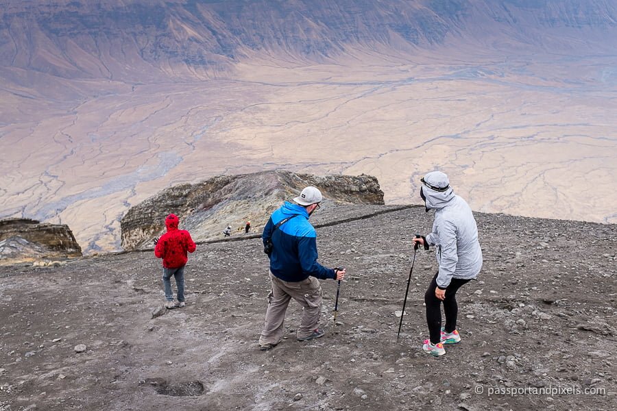 Group of hikers descending Ol Doinyo Lengai Mountain with trekking poles on rocky terrain.