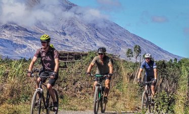 Three mountain bikers riding on a trail with a mountain in the background under a clear sky.