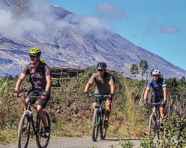 Three mountain bikers riding on a trail with a mountain in the background under a clear sky.