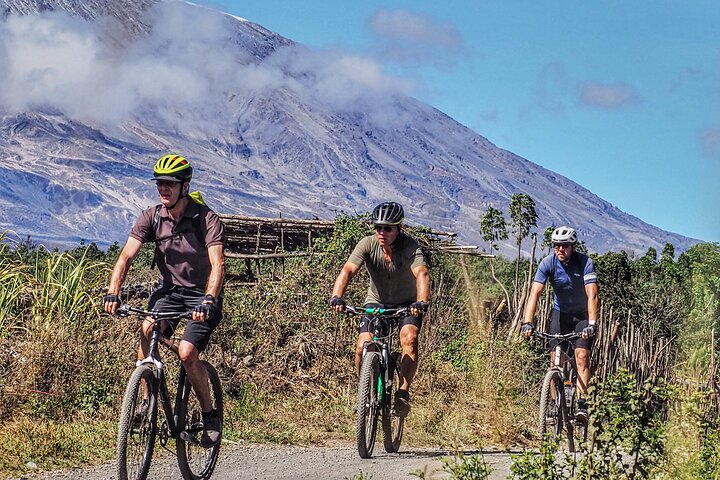 Three mountain bikers riding on a trail with a mountain in the background under a clear sky.