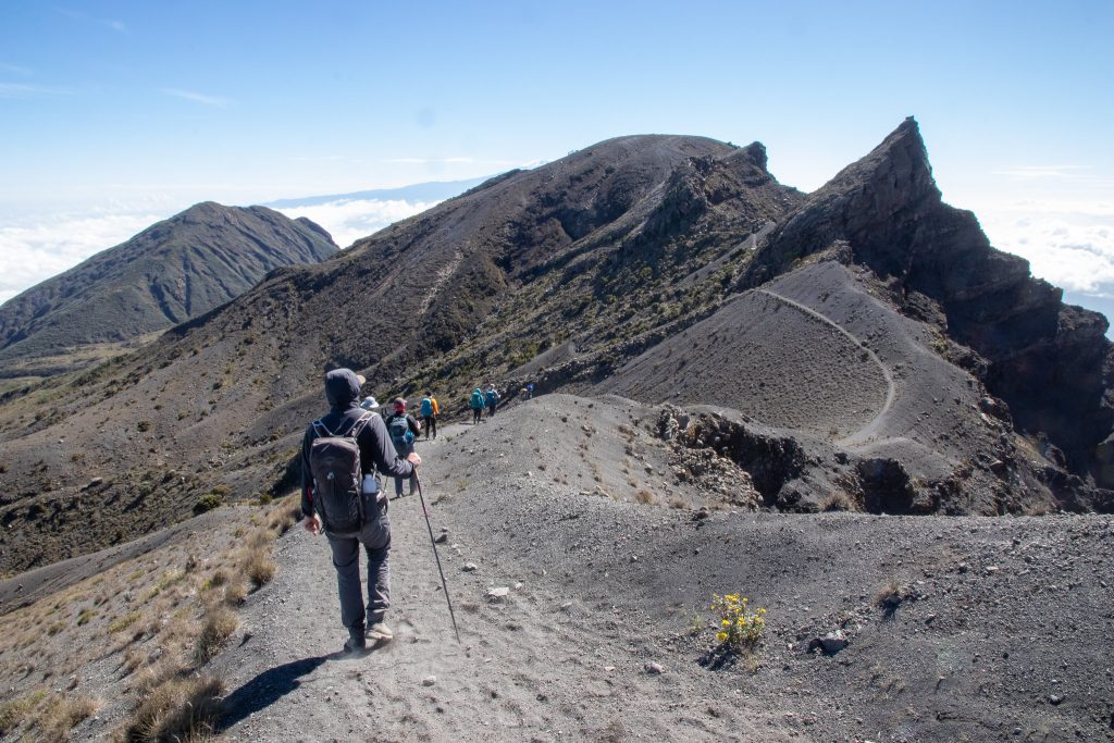 Group of hikers ascending a rugged mountain trail with rocky terrain and clear skies.