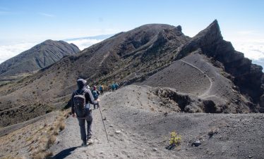 Group of hikers ascending a rugged mountain trail with rocky terrain and clear skies.