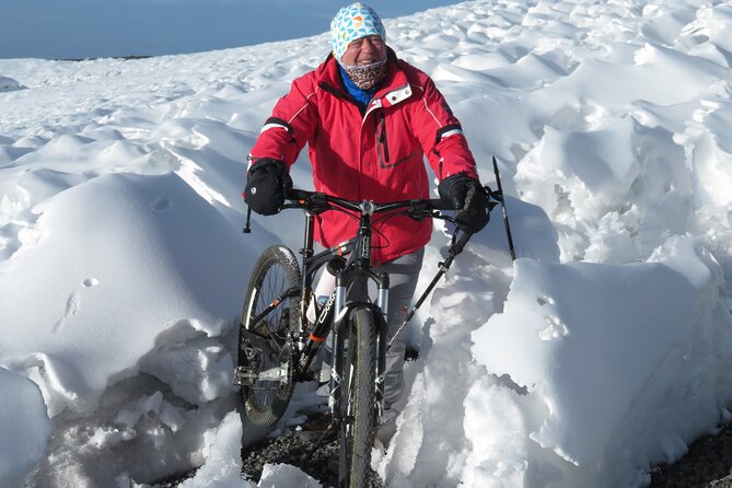 Individual in a red jacket and colorful hat maneuvering a bicycle through snow-covered terrain.