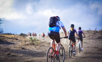 Group of mountain bikers riding on a dirt trail through a hilly landscape under a cloudy sky.