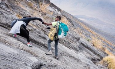 Two climbers navigating a steep rocky slope, one assisting the other with a handhold.