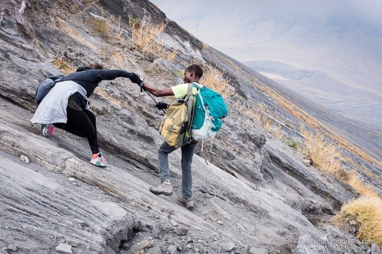 Two climbers navigating a steep rocky slope, one assisting the other with a handhold.