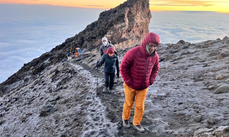 Group of hikers climbing the rocky trail of Mount Meru during sunrise with clouds below.