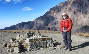 Person standing at Hindu Point 3300 summit with rocky terrain and mountains in the background.