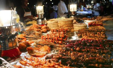 Grilled seafood, spiced snacks and stacked flatbreads fill a lively Stone Town spice tour market stall at night in Zanzibar.
