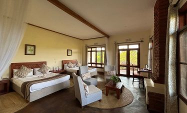 A spacious safari lodge suite features twin beds, woven rugs, lounge chairs, a brick fireplace and wide windows with garden views.