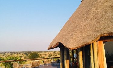 A thatched safari lodge deck at Mara Mara Tented Lodge looks out over the Serengeti plains, with wooden seating and warm evening light.