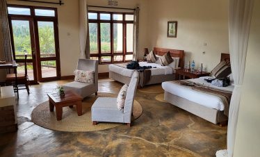 A spacious Marera Valley Lodge suite shows twin beds, lounge chairs, a low coffee table and large windows looking onto green grounds in warm daylight.