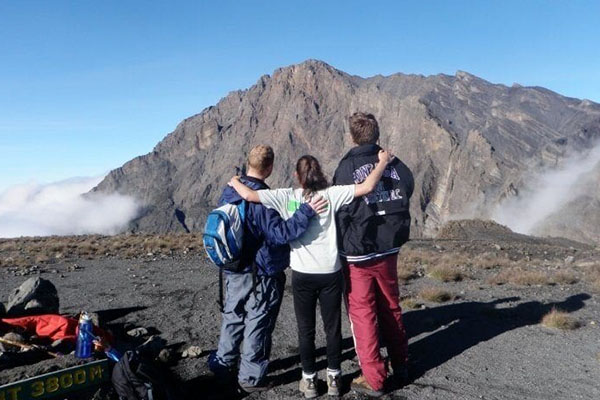 Three hikers standing together with arms around each other, overlooking the Meru Hills landscape.