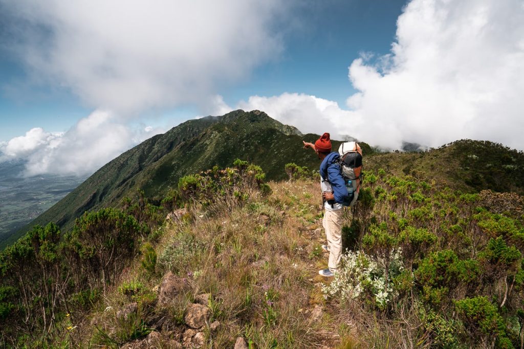 Person standing on a mountain ridge with a backpack, overlooking a scenic view in Tanzania.