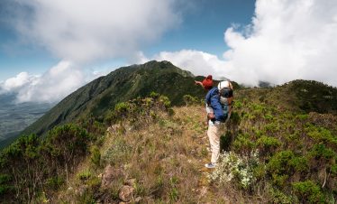 Person standing on a mountain ridge with a backpack, overlooking a scenic view in Tanzania.