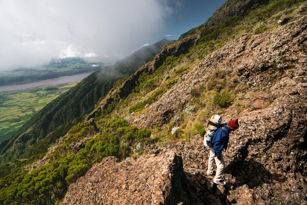 Person hiking on rocky terrain of Mount Hanang with a view of the landscape below in Tanzania.