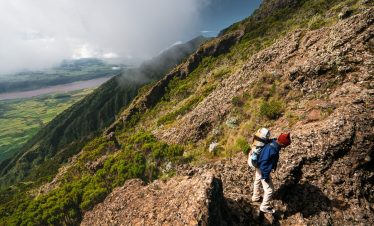 Person hiking on rocky terrain of Mount Hanang with a view of the landscape below in Tanzania.