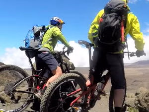 Two mountain bikers in bright gear overlooking a landscape near Kilimanjaro.