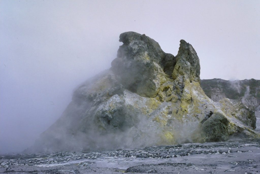 Volcanic rock formation with yellow and gray hues at Ol Doinyo Lengai, surrounded by mist.