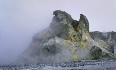 Volcanic rock formation with yellow and gray hues at Ol Doinyo Lengai, surrounded by mist.