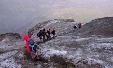 Group of hikers climbing the Ol Doinyo Lengai volcano in Tanzania, with a rugged landscape in the background.